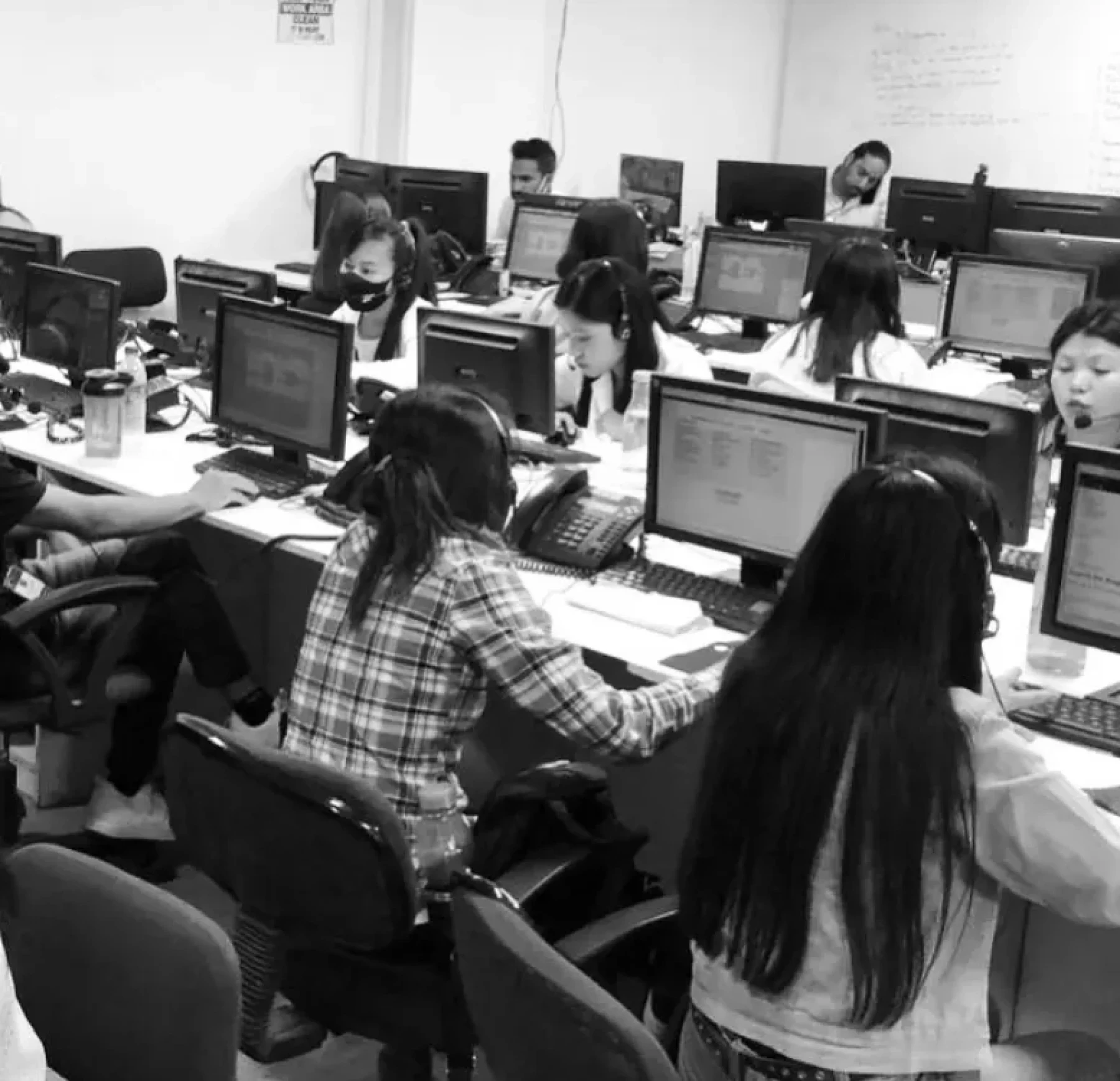 Black-and-white office photo showing RHI support agents working at desks with computers and headsets.